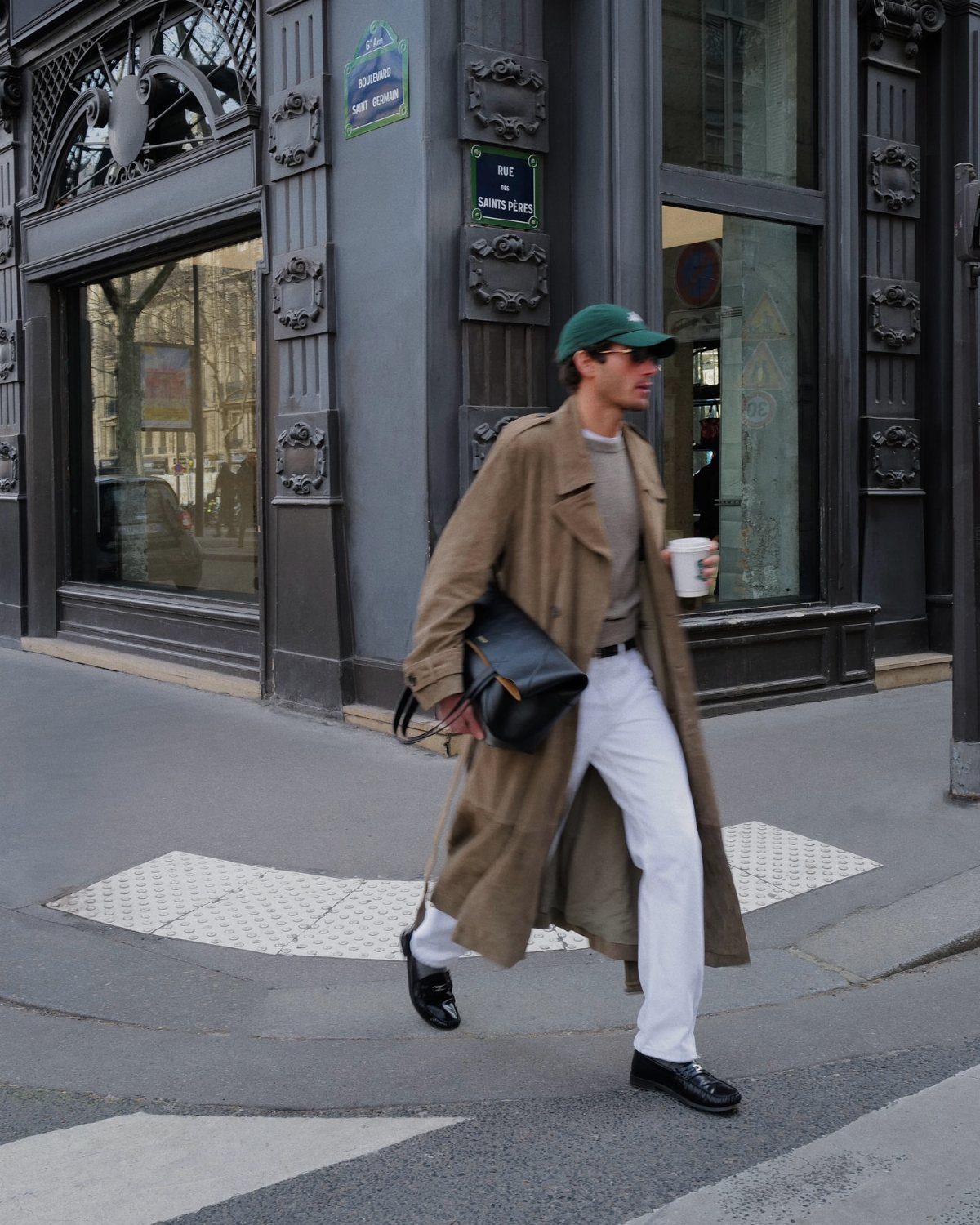 Man walking in a tan suede trench coat, white pants, and green cap.