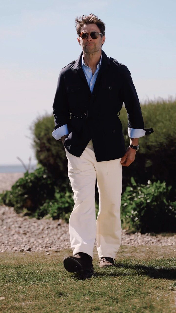 Man wearing a navy lightweight jacket, blue shirt, and white trousers outdoors.