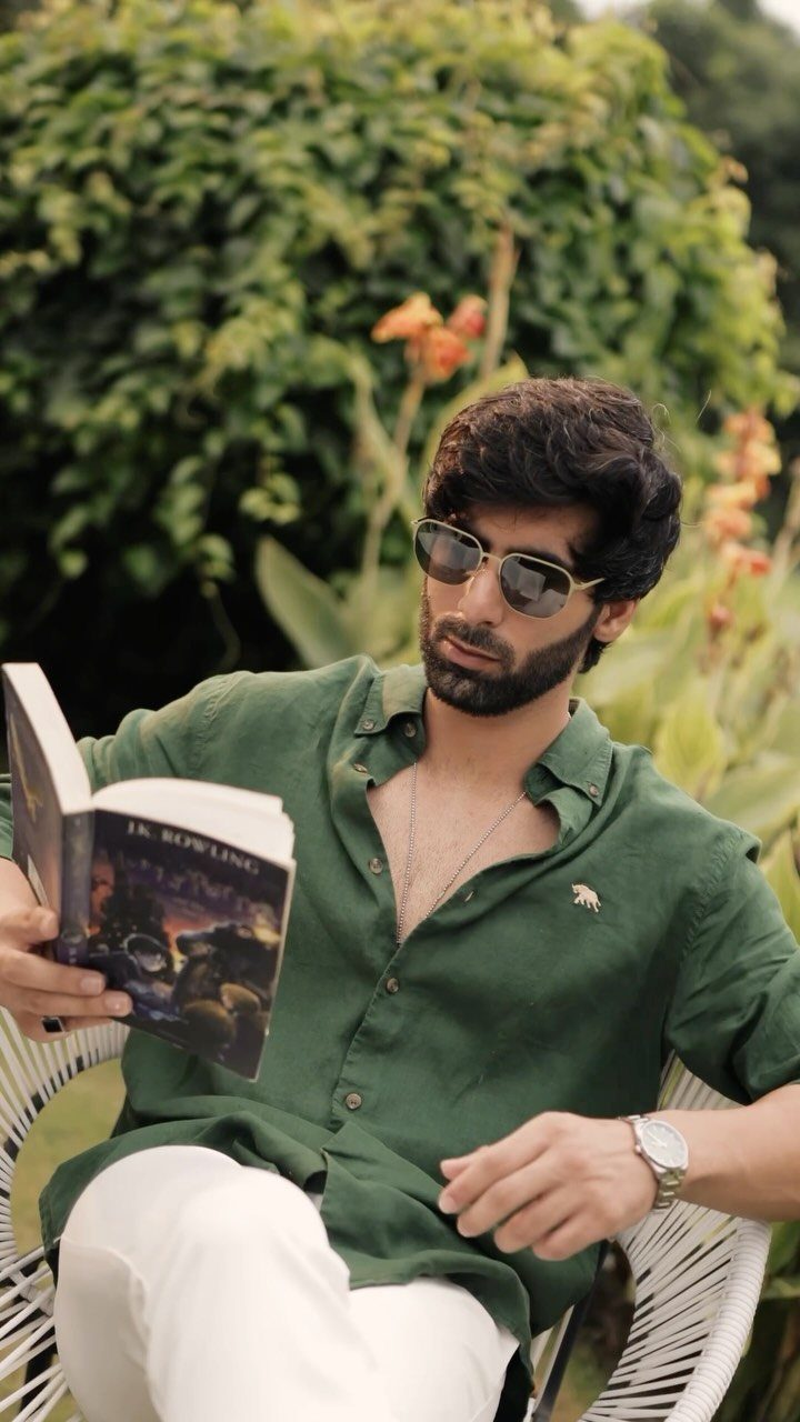 Man in green linen shirt and white pants reading a book outdoors.