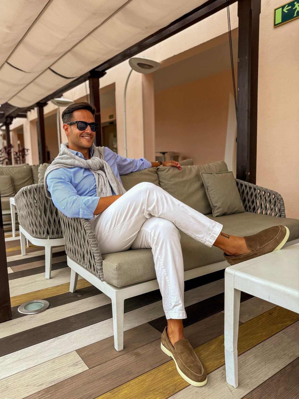 Man in white trousers and brown suede loafers sitting on an outdoor sofa.