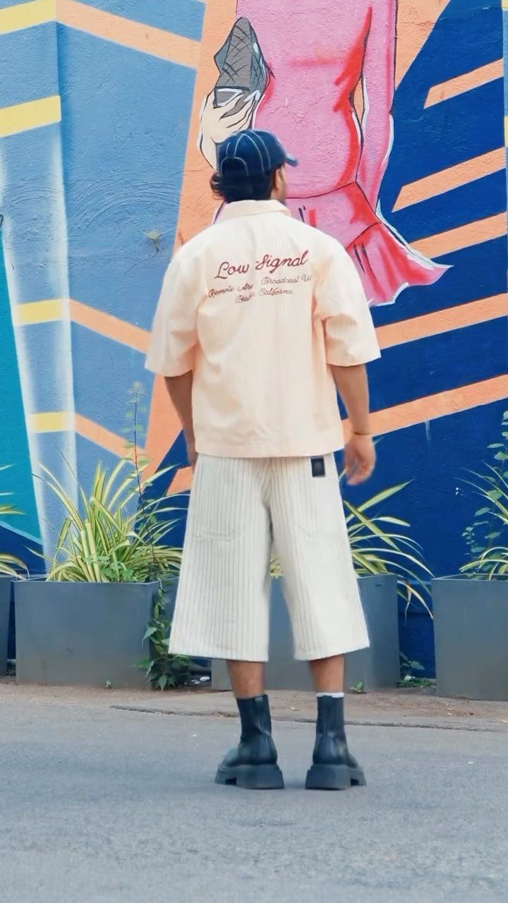Man in peach shirt and wide cream trousers wearing chunky black boots.