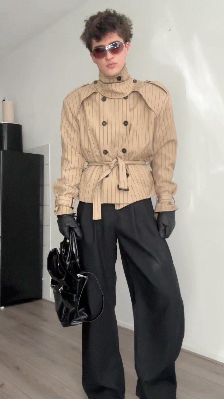 Person wearing a tan pinstriped trench coat buttoned to the top and black trousers.