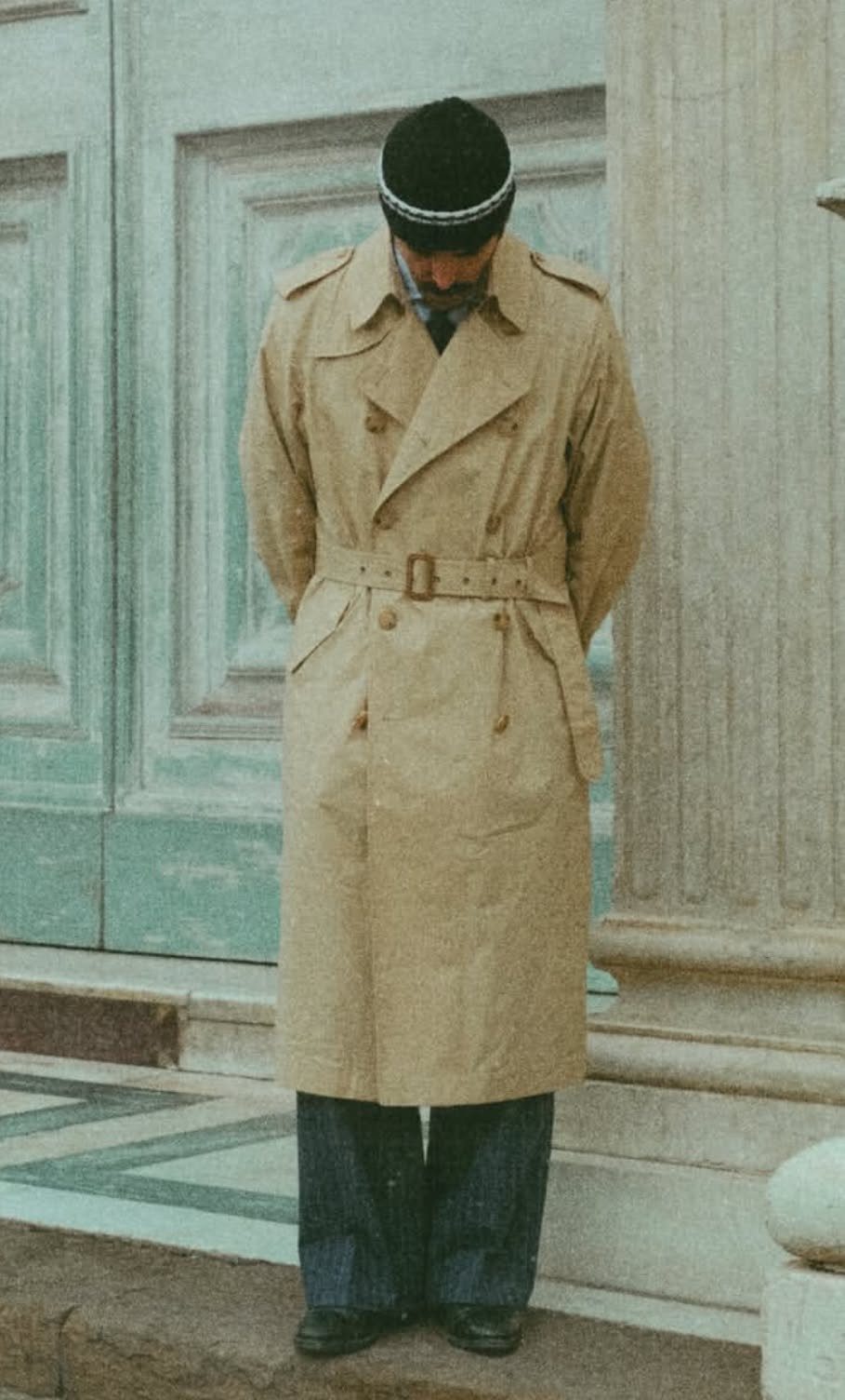 Man in a tan trench coat buttoned to the top and a black beanie.