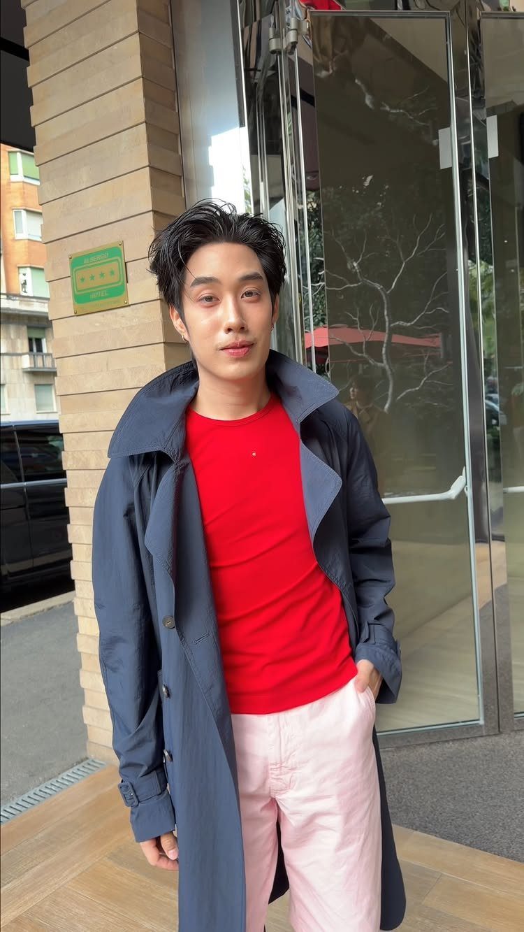 Man wearing a dark blue trench coat, red t-shirt, and pink chinos outdoors.