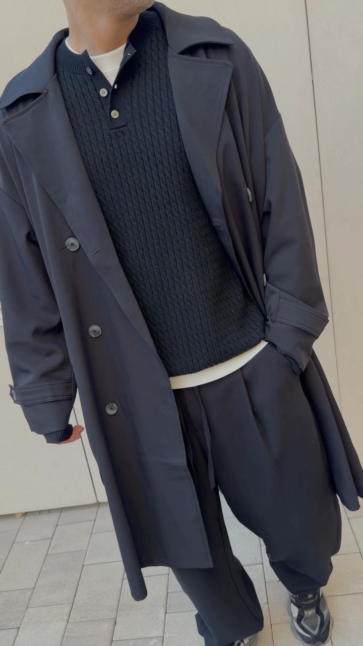 Person wearing a navy trench coat with a black ribbed knit polo sweater.