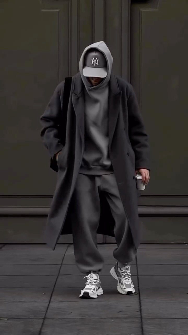 Person in a gray overcoat, hoodie, sweatpants, and white sneakers in street style.