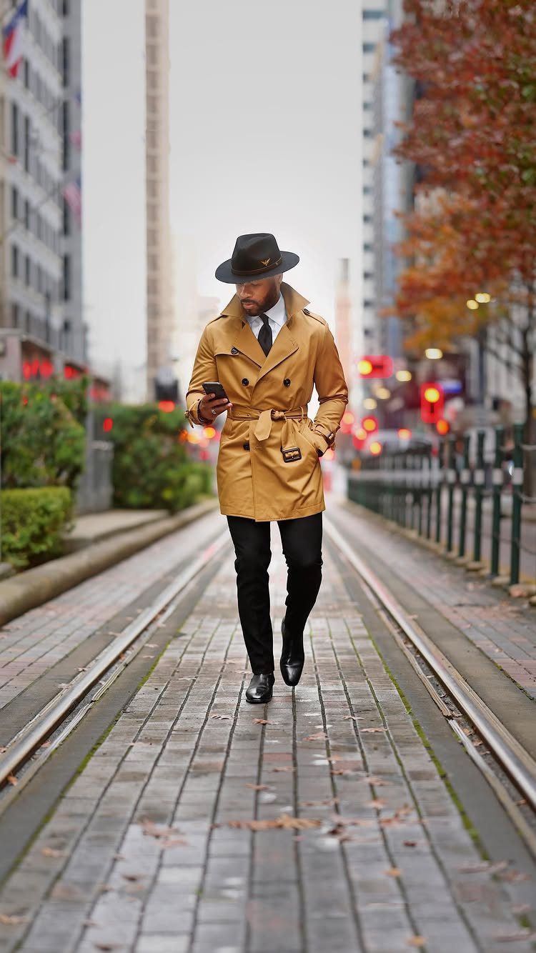 Man in tan trench coat and black fedora walking on city street