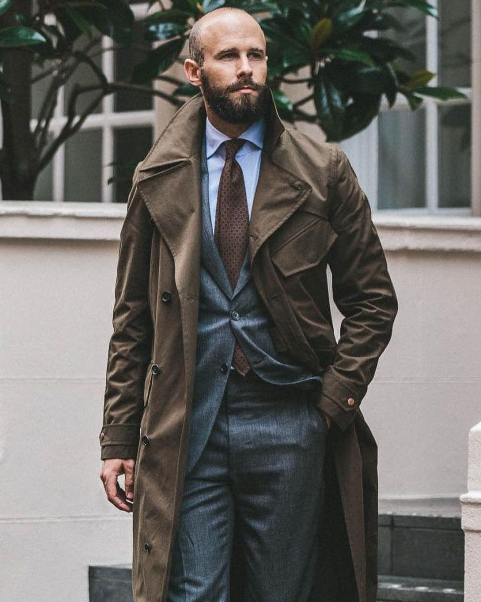 Man wearing a brown trench coat over a grey three-piece suit and tie.