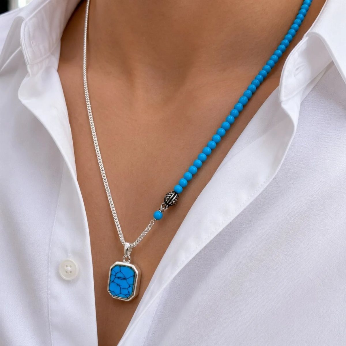 Turquoise pendant on silver chain and blue beaded necklace over white shirt