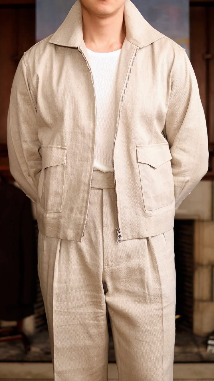 Person wearing a light beige linen jacket and matching pleated trousers indoors.