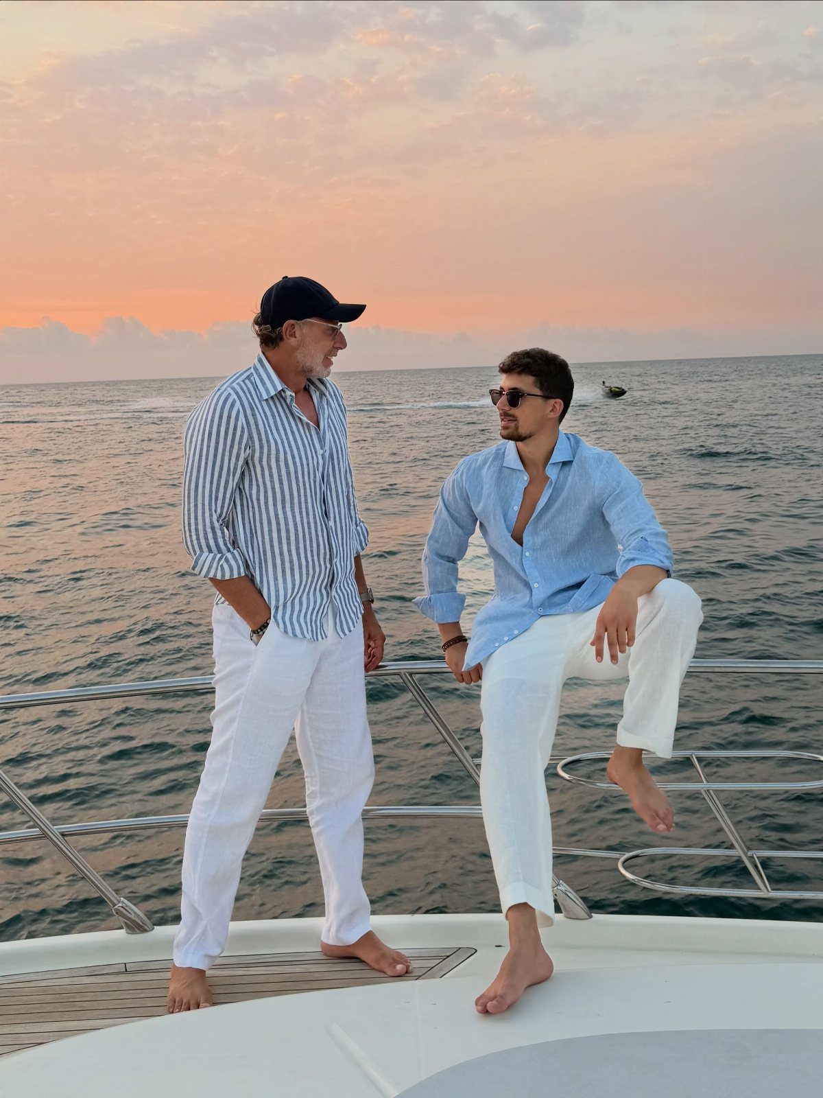Two men in summer shirts and white trousers standing on a boat deck.