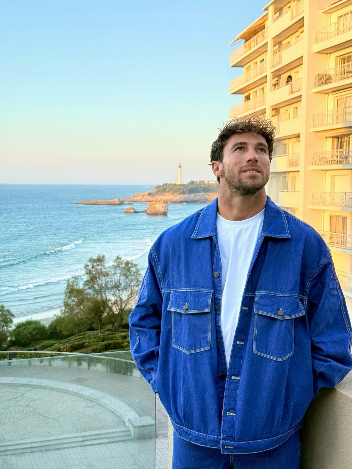 Man in blue denim jacket and white t-shirt on a coastal balcony