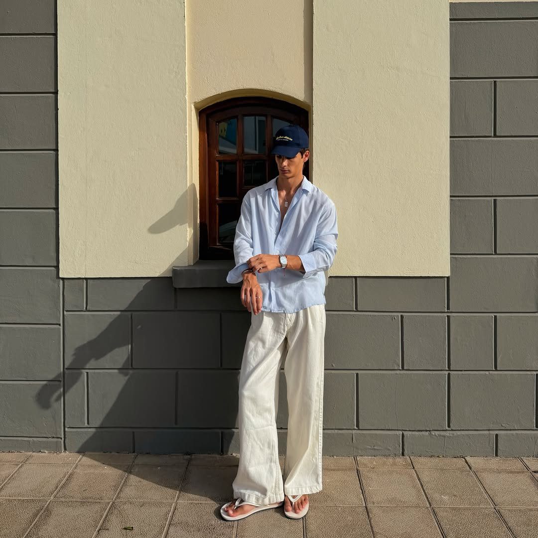 Man wearing a light blue linen shirt and wide white trousers outdoors.
