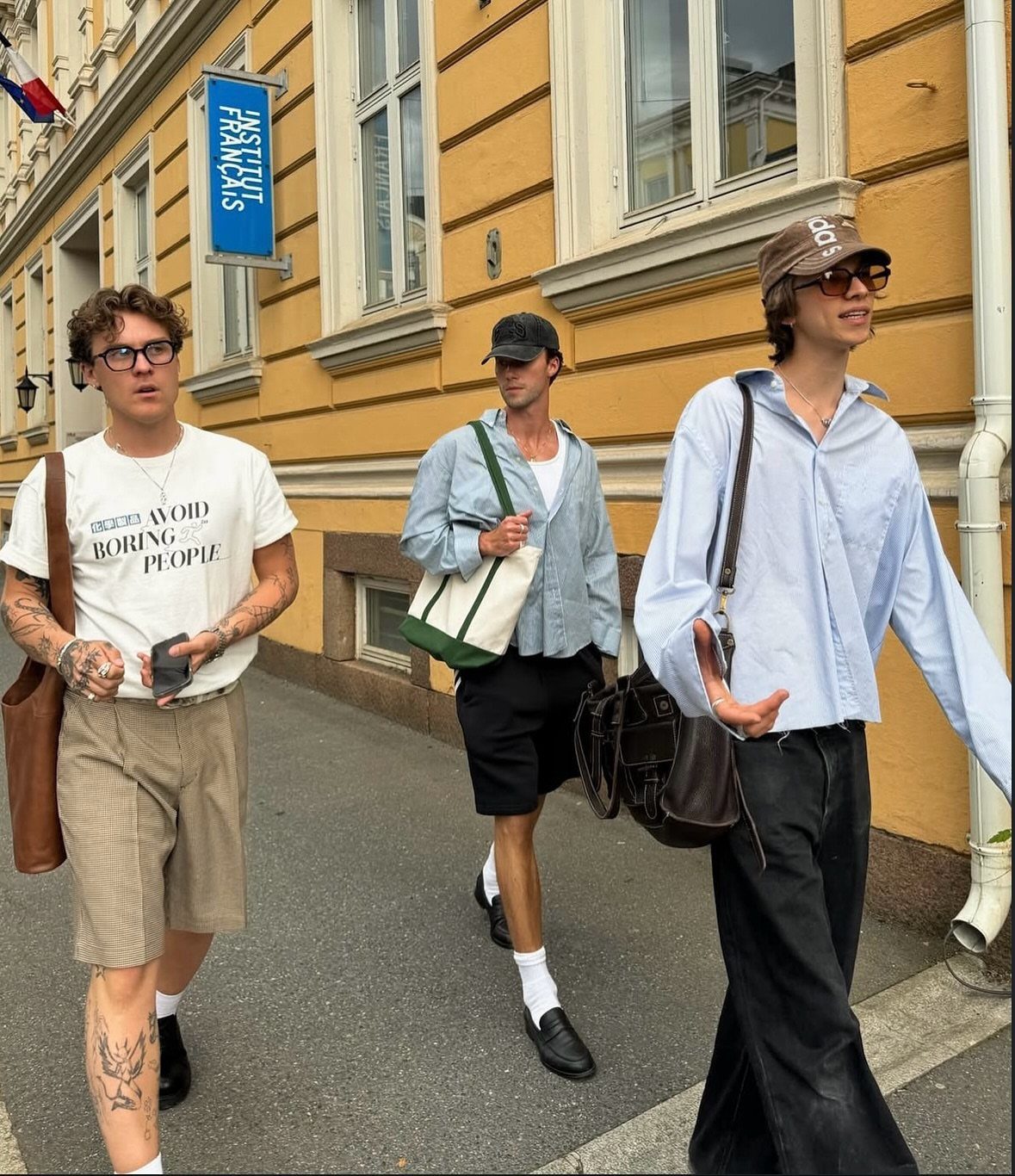 Three men walking on a city street wearing various trendy summer outfits.