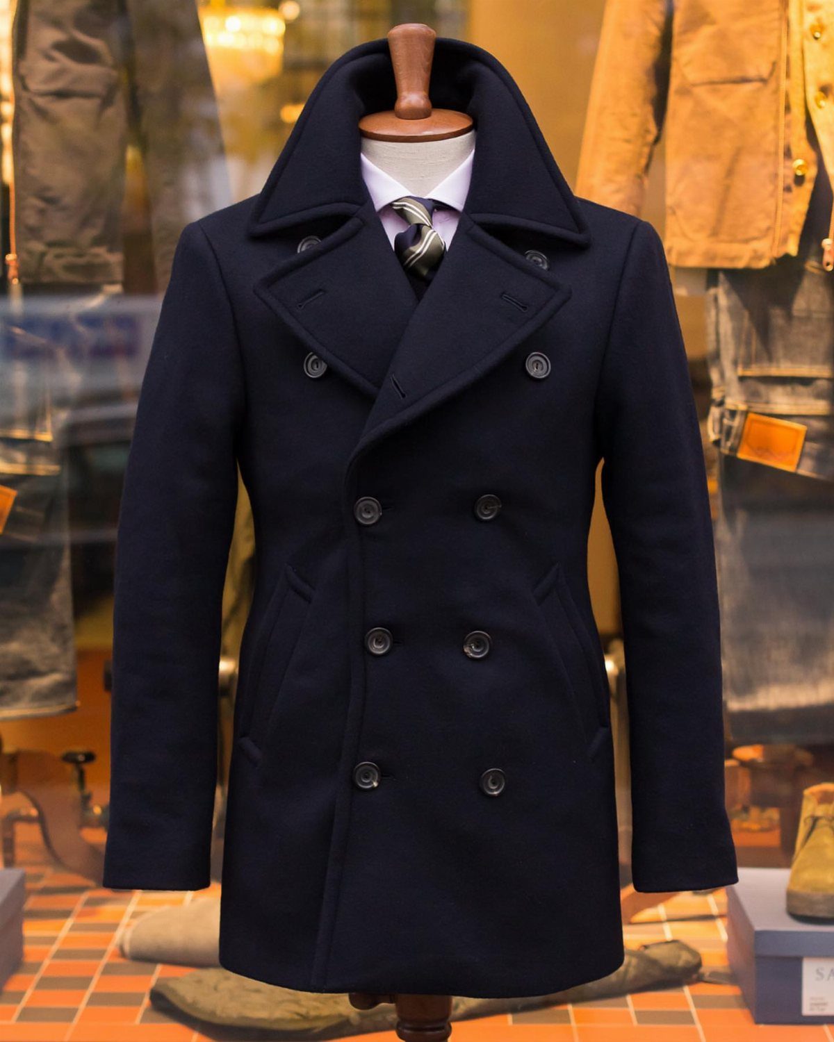 Navy blue double-breasted overcoat on a mannequin with a shirt and tie.