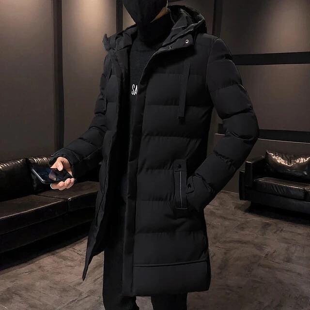 Man wearing a long black quilted puffer coat with a hood indoors