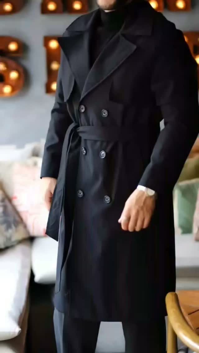 Man wearing a classic black double-breasted trench coat with a belted waist.