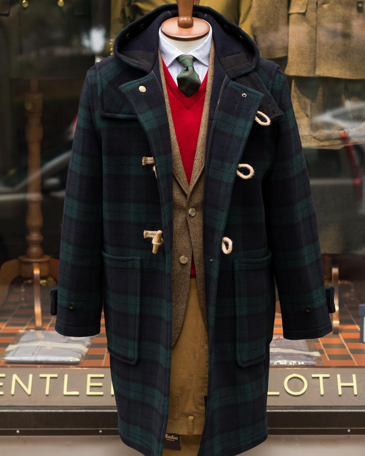 Dark green plaid duffle coat with toggles on a mannequin in a storefront
