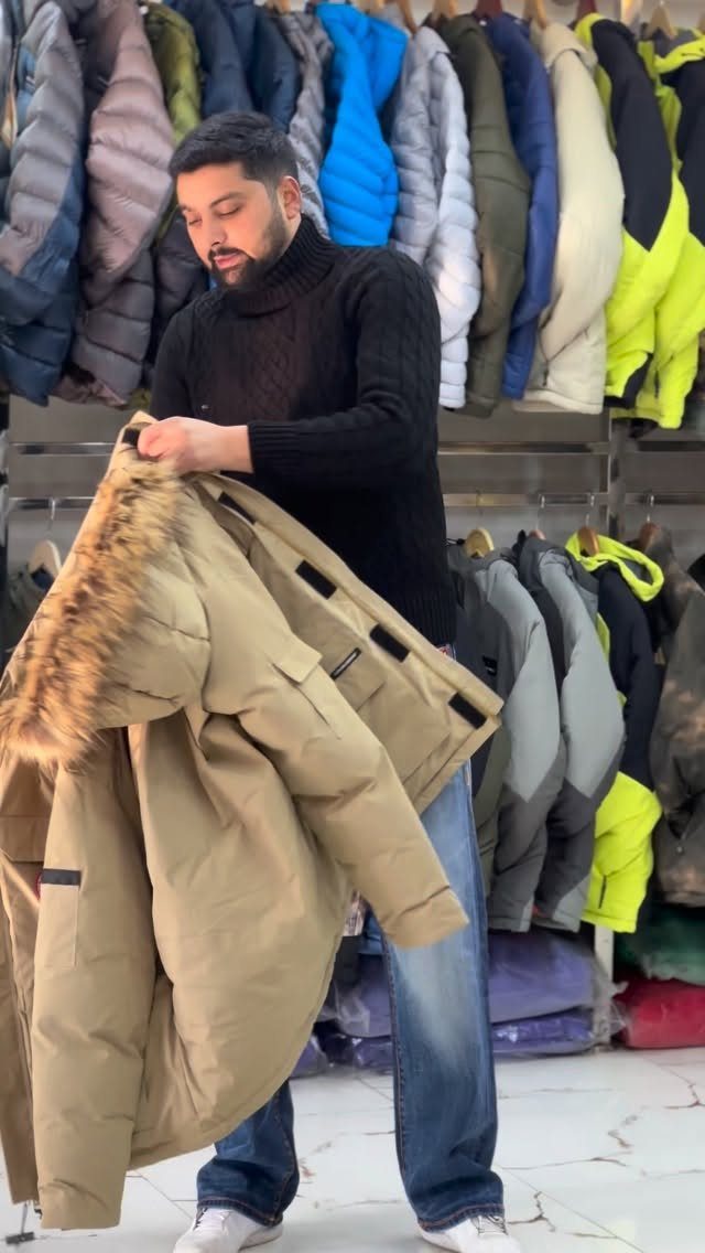Man holding a tan parka with a fur-trimmed hood in a clothing store