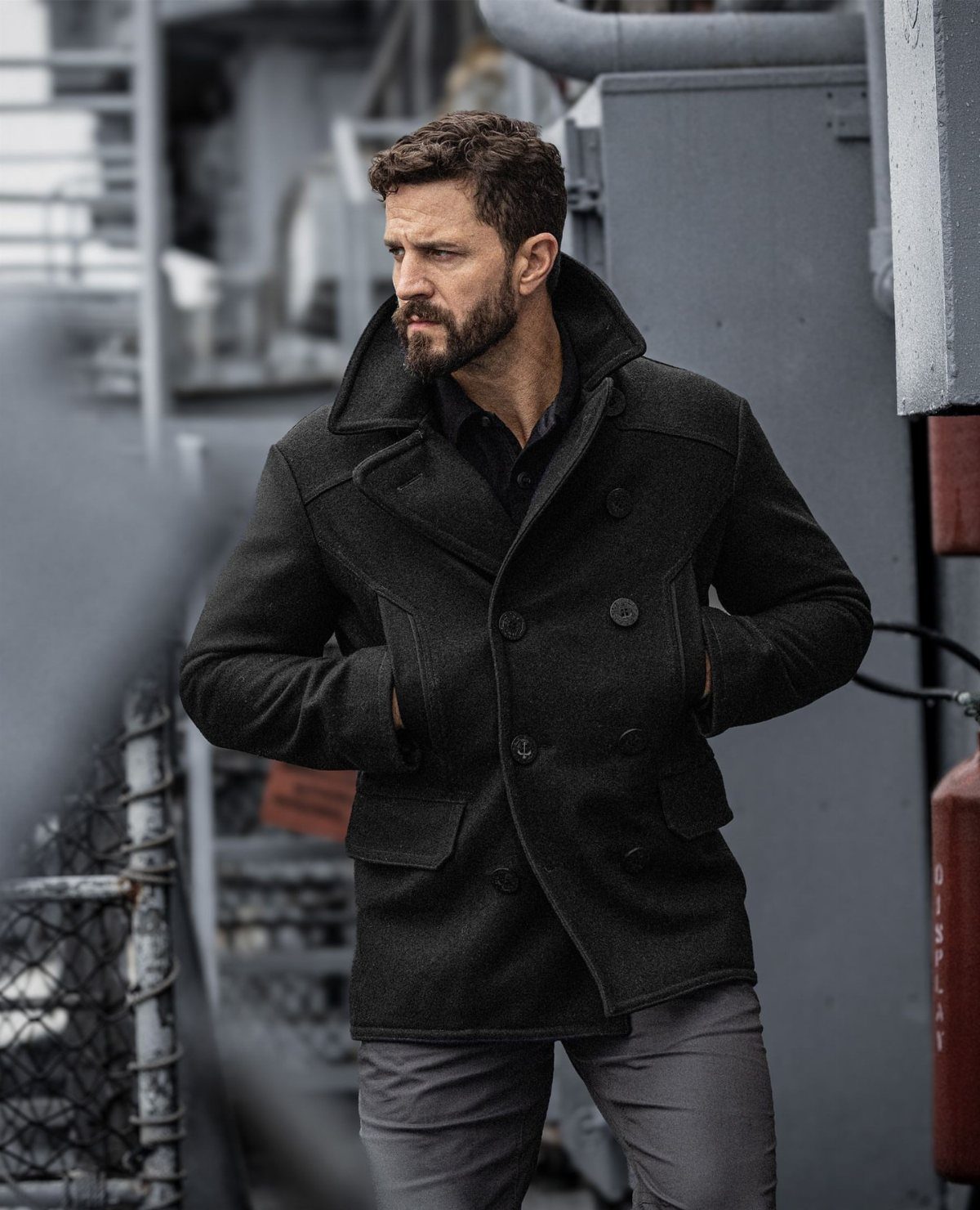 Man wearing a dark grey double-breasted wool peacoat on a ship deck.