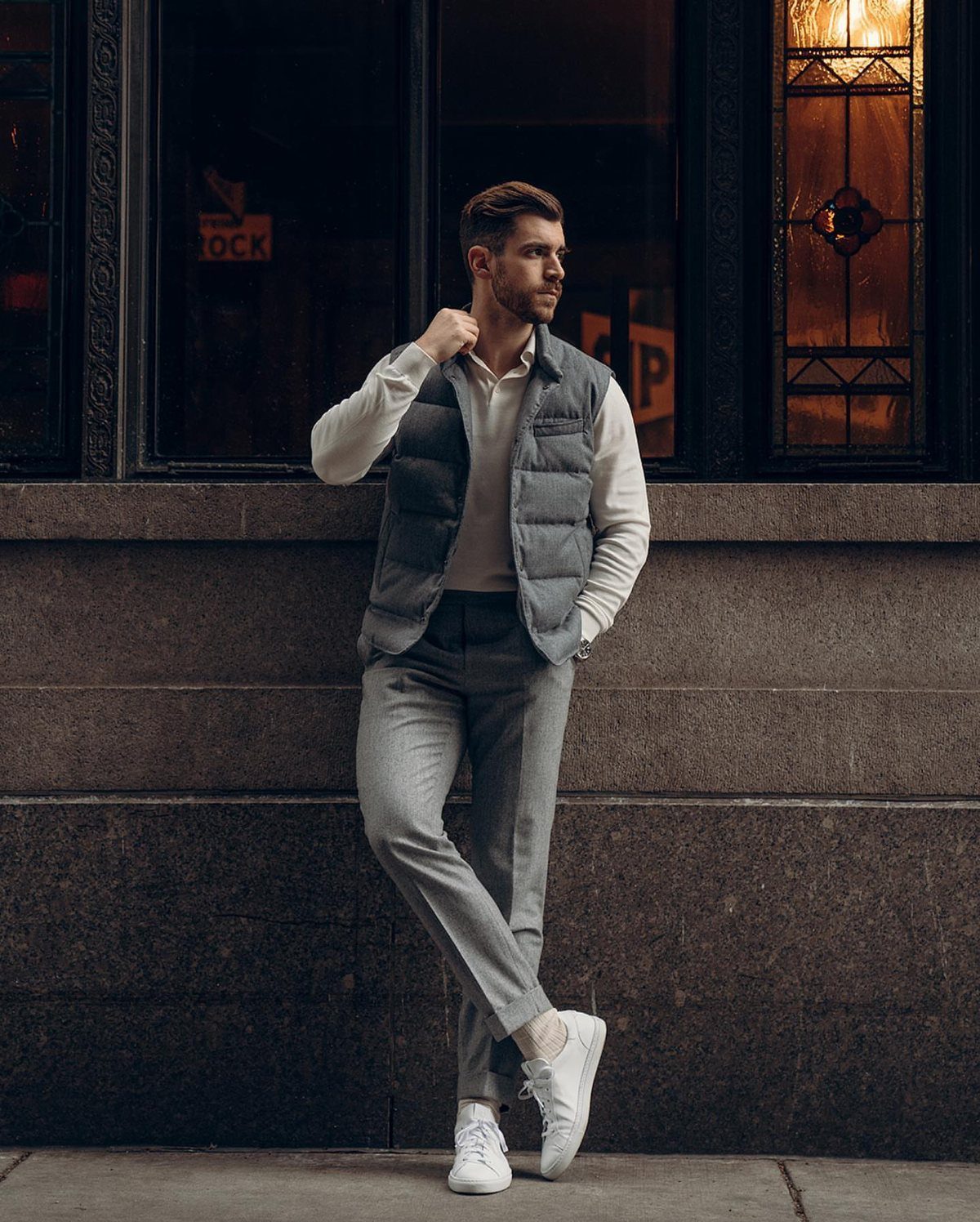 Man wearing a grey puffer vest over a white shirt and grey trousers.