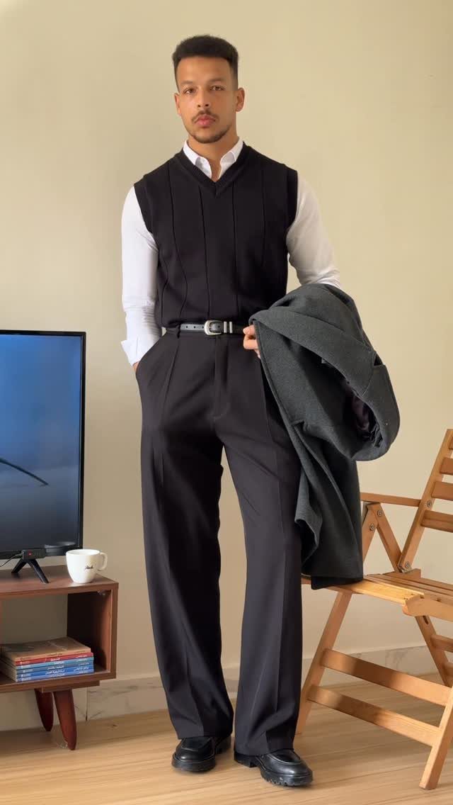 Man wearing a black sweater vest over a white shirt and black trousers.
