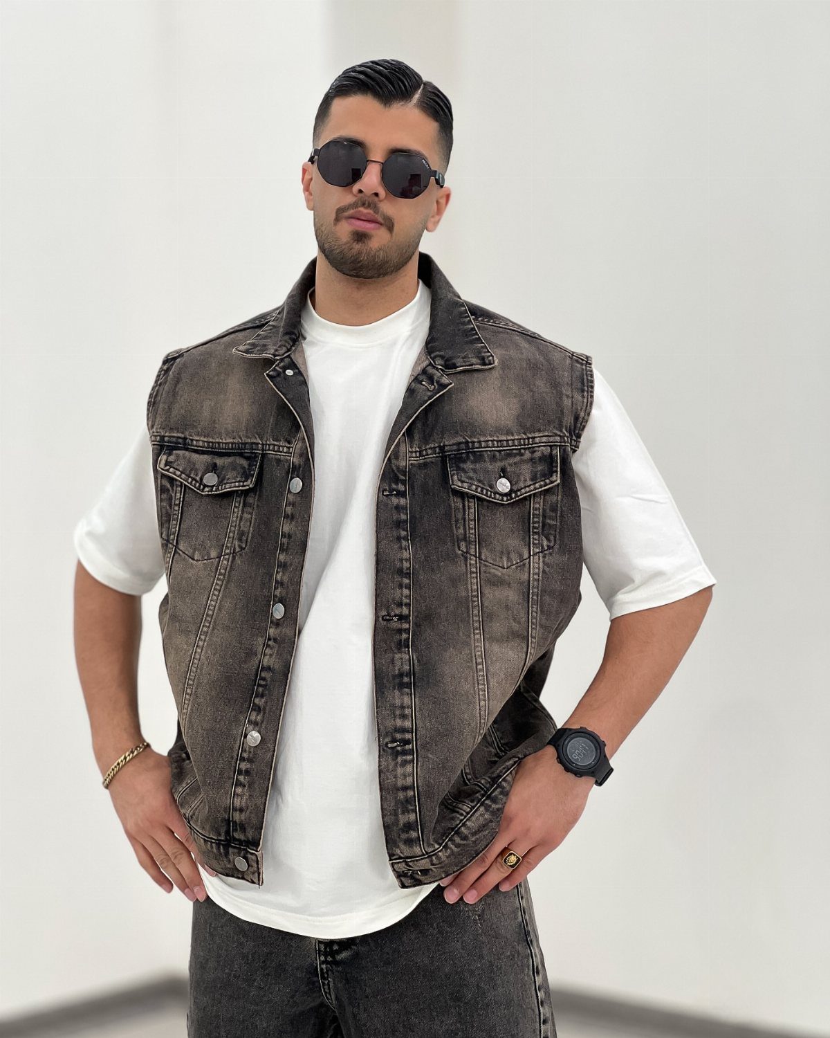 Man wearing a dark grey denim vest over a white t-shirt and jeans.