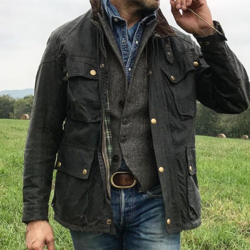 Man wearing a grey tweed vest layered under a dark field jacket and jeans.