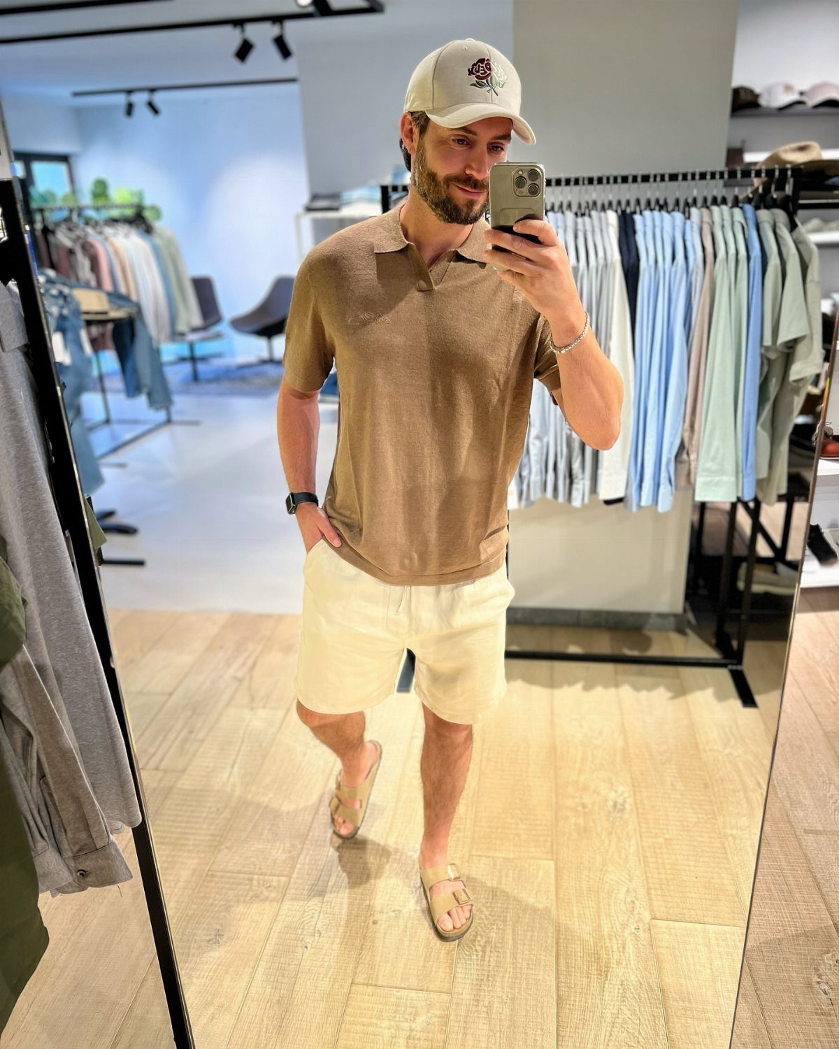 Man in tan polo, white shorts, and baseball cap posing in clothing store
