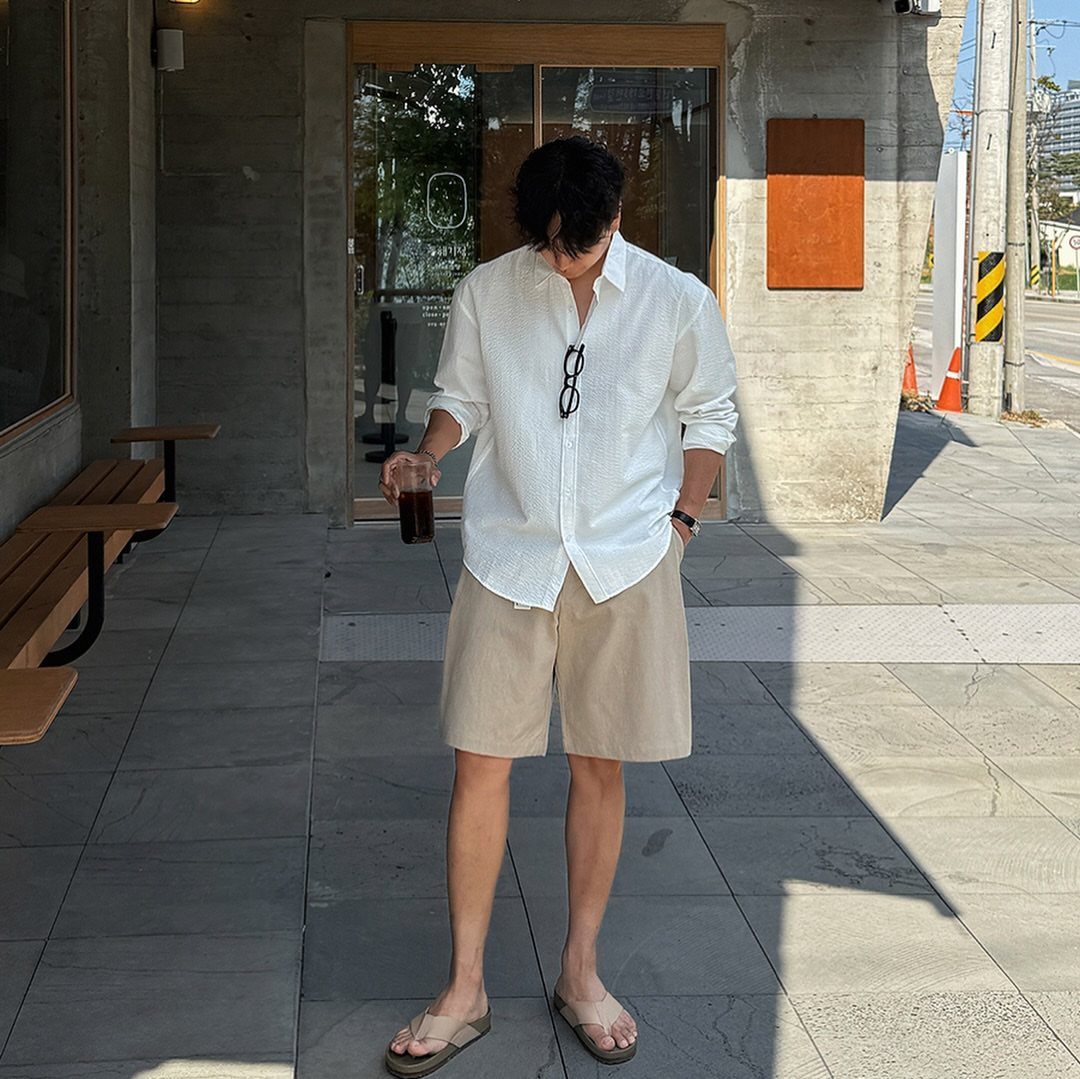 Man wearing a white button-down shirt and beige shorts standing outside a building.