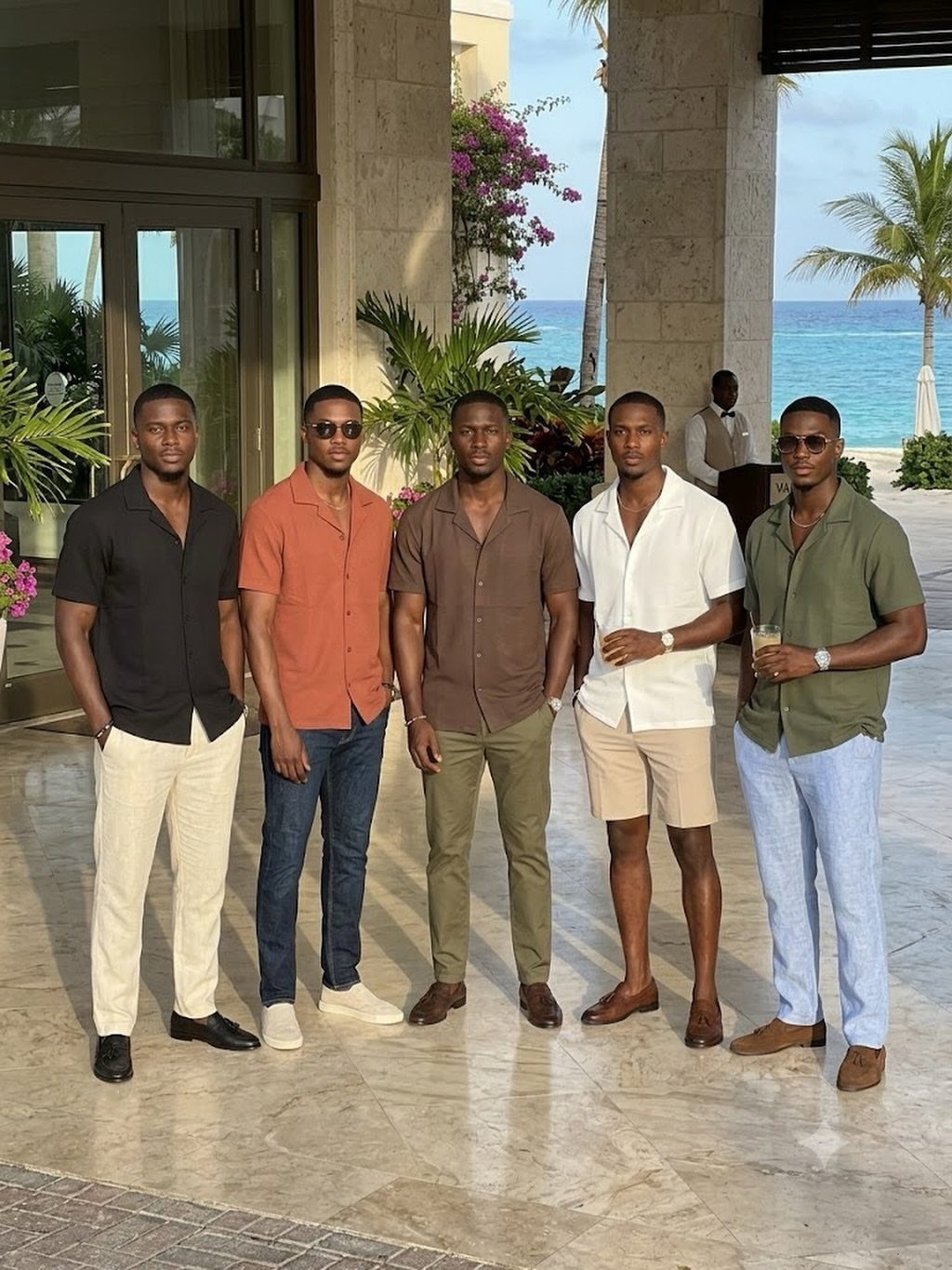 Five men posing in colorful summer shirts and light trousers on a patio.