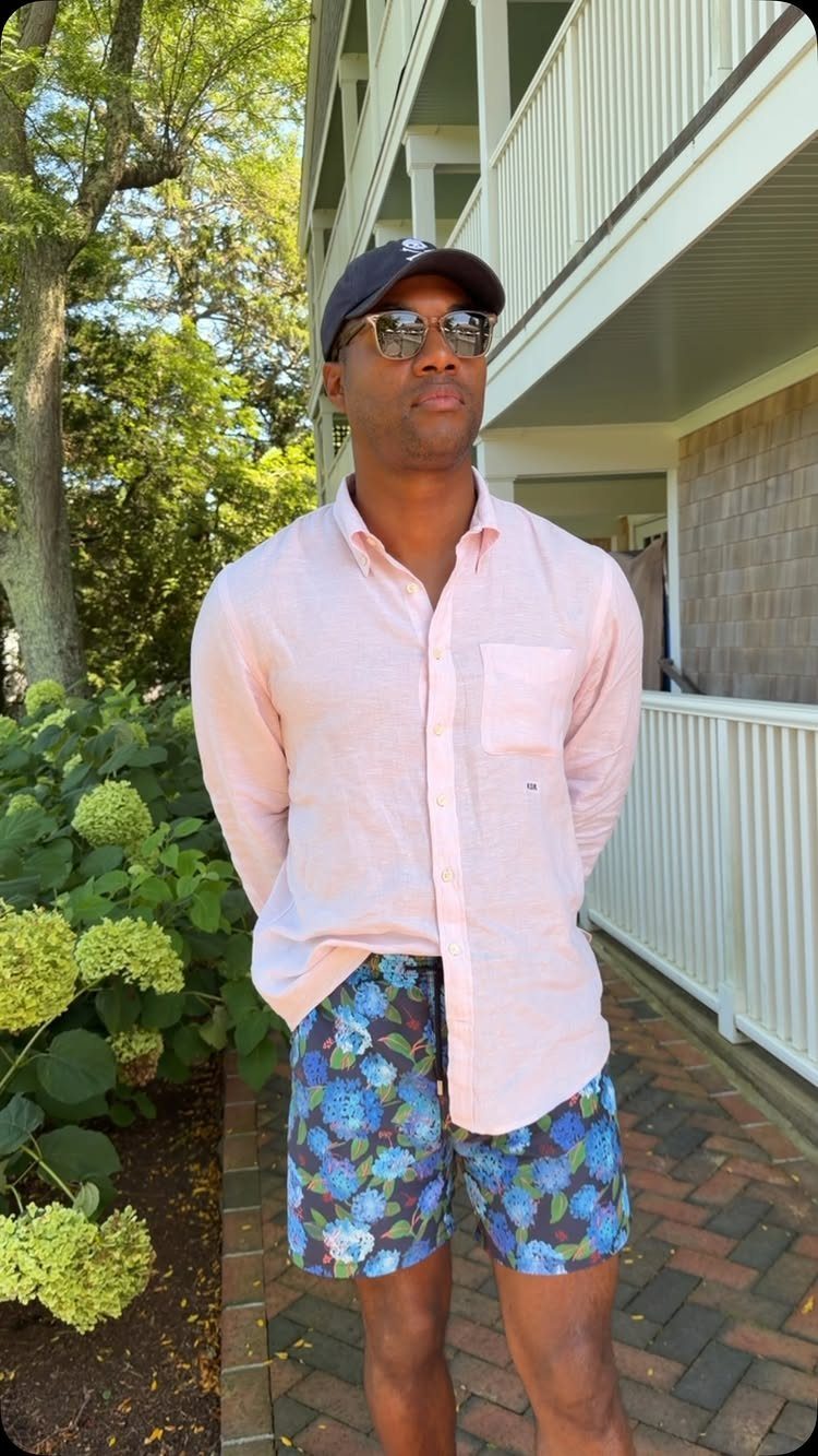 Man wearing a pink linen shirt and blue floral swim trunks outdoors.