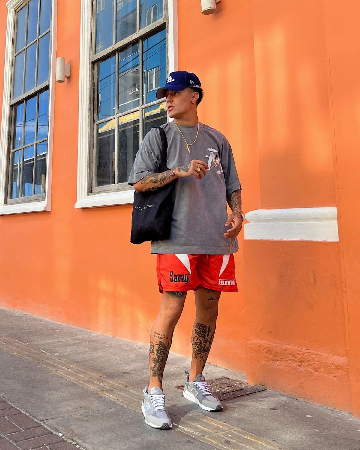 Man in grey t-shirt and red shorts posing against an orange wall.