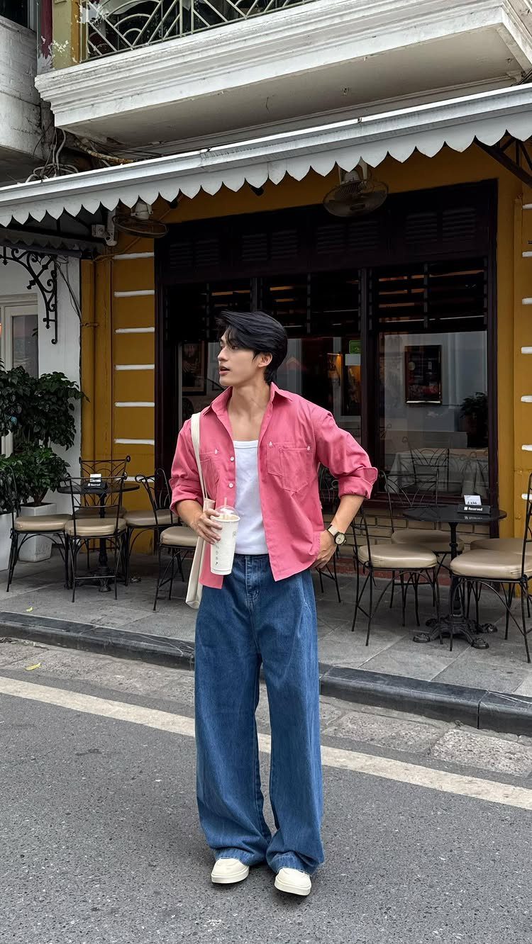 Man in pink shirt and wide-leg blue jeans standing on a city street