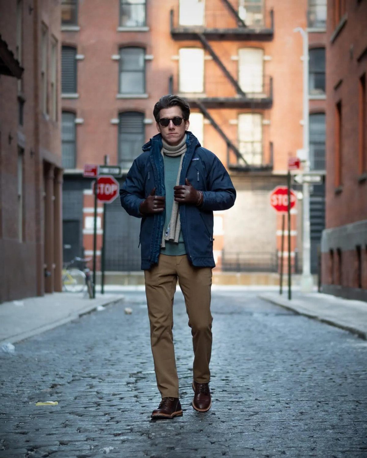 Man in navy blue parka and tan trousers walking on cobblestone city street