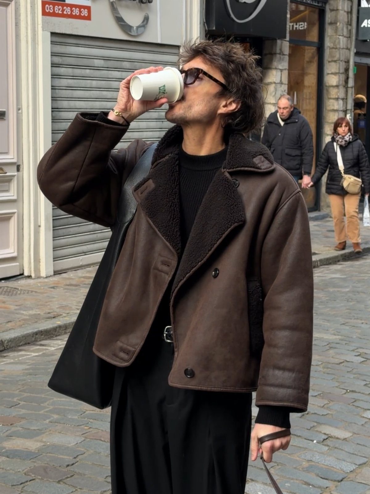 Man in brown leather shearling jacket drinking coffee on a cobblestone street