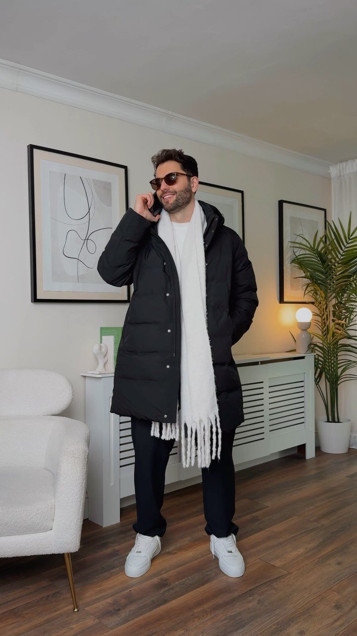 Man in a long black puffer jacket and white scarf talking on phone indoors