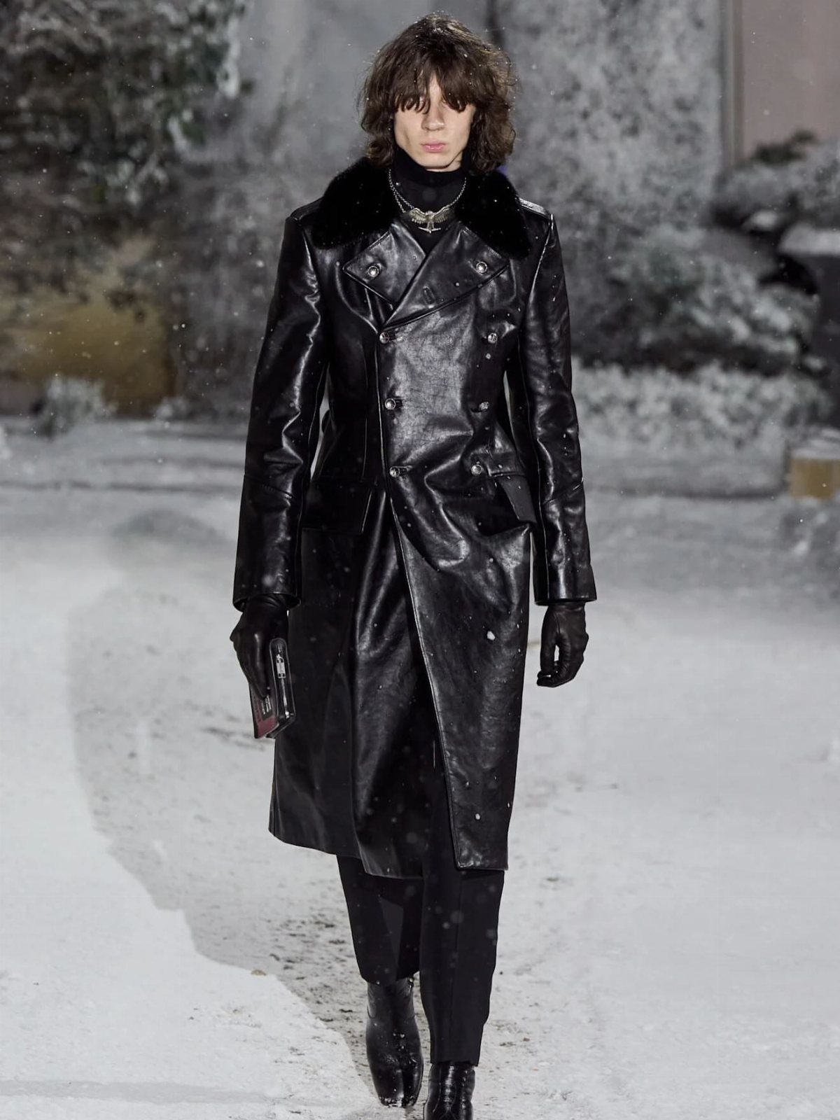 Person wearing a long black leather coat with fur collar walking in snow
