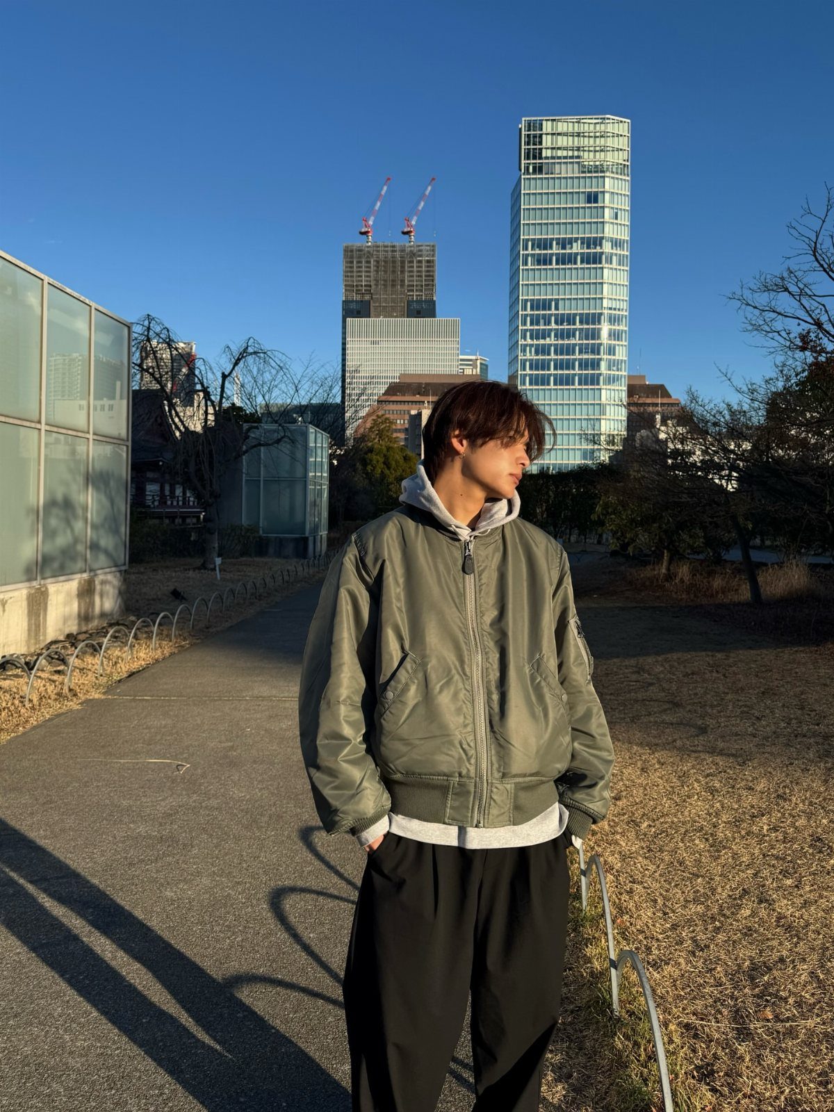 Man wearing olive green bomber jacket and grey hoodie in urban city setting
