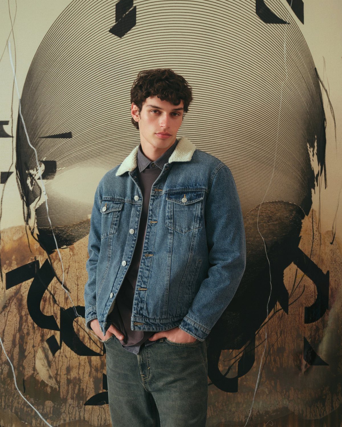 Man wearing a blue denim jacket with sherpa collar and grey jeans.