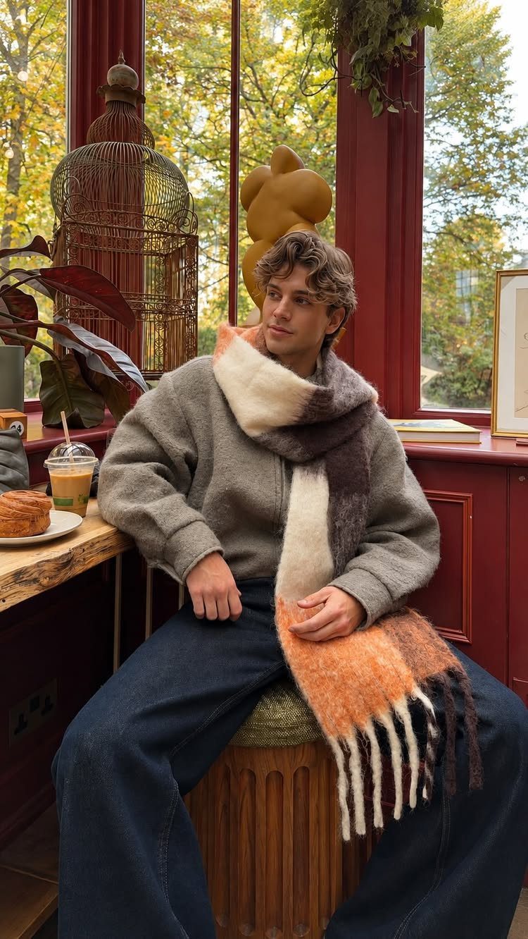 Young man wearing a grey sweater and colorful scarf sitting by a window