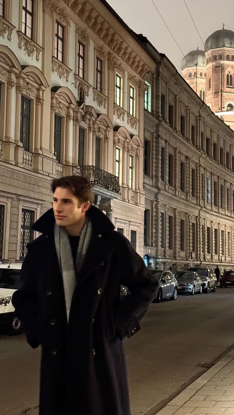 Man in a long black wool coat and grey scarf on a city street