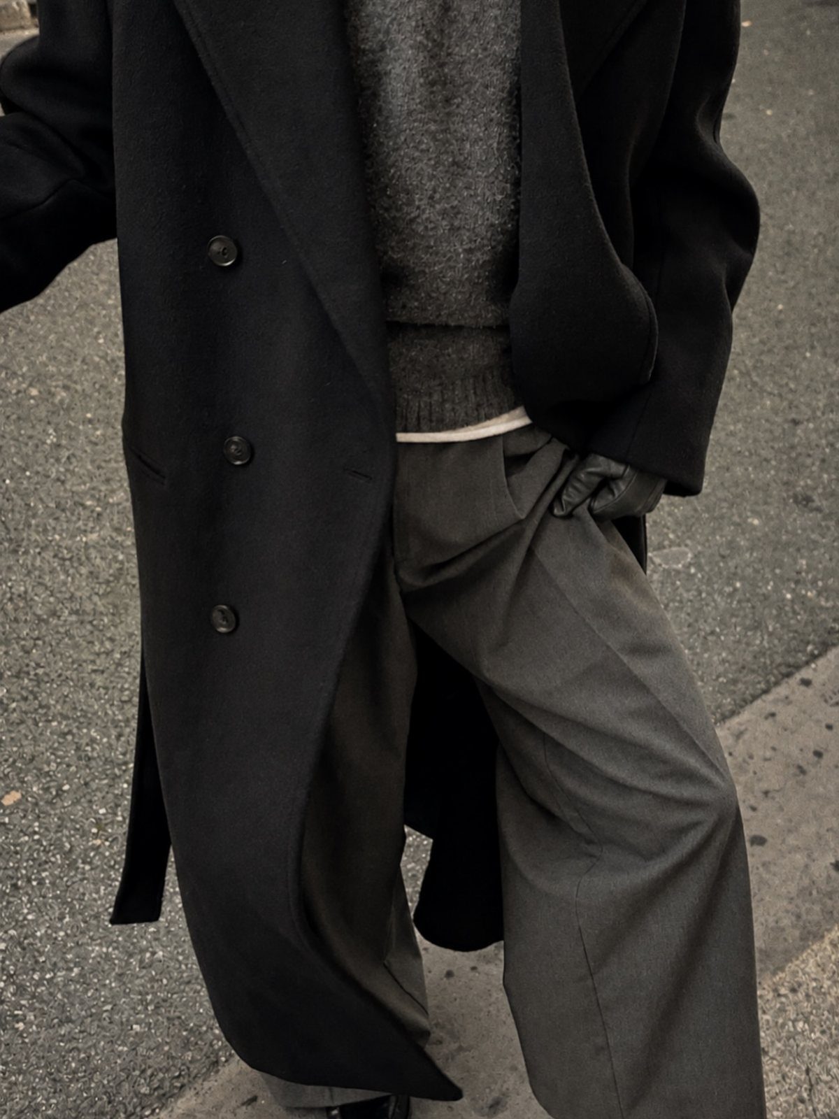 Person wearing a black wool overcoat, grey sweater, and grey trousers on a street