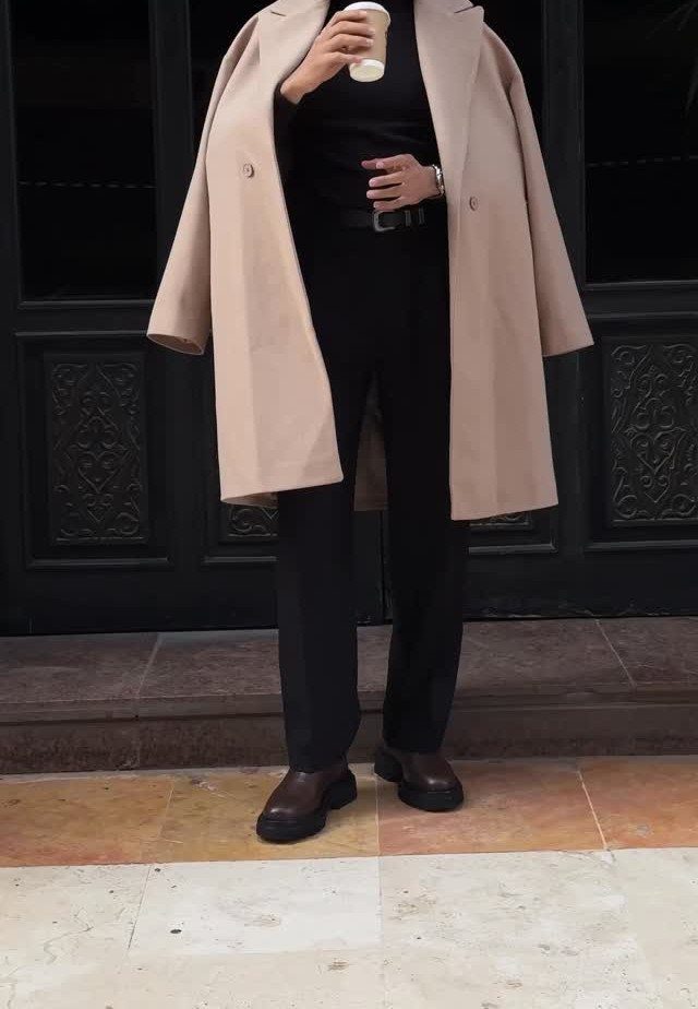 Person wearing a camel wool overcoat with black trousers and brown boots