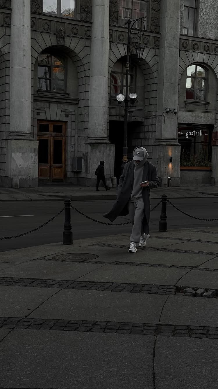 Person wearing a long dark wool coat and white beanie walking in city