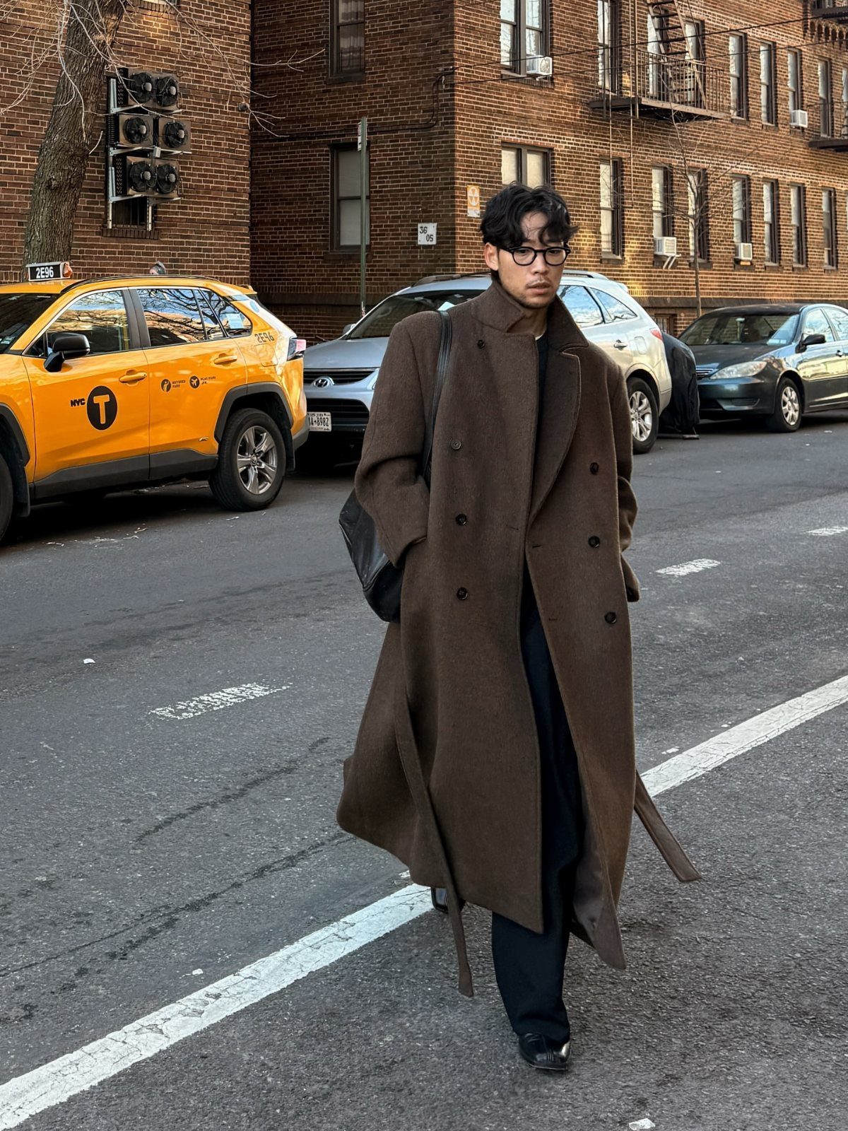 Man wearing a long brown wool overcoat and black trousers on a city street