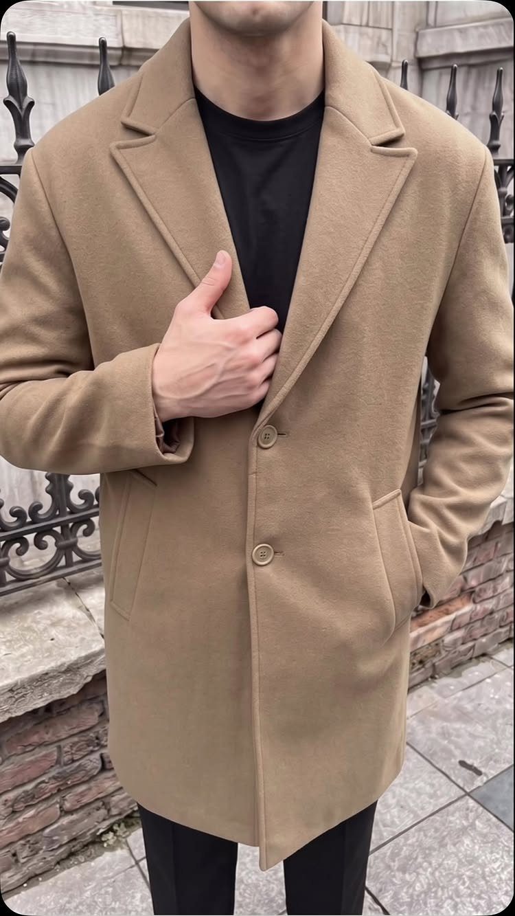 Man wearing a tan wool overcoat with a black shirt and trousers.