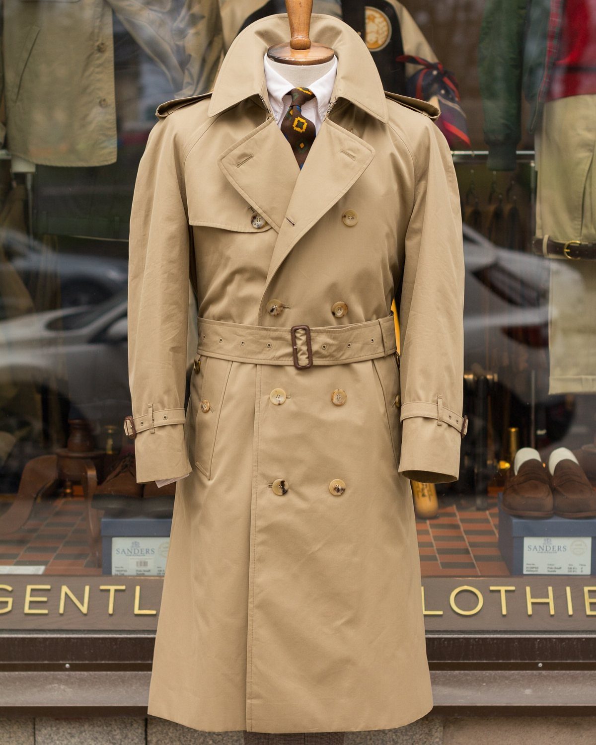 Tan double-breasted trench coat with belt displayed on a mannequin in a shop window