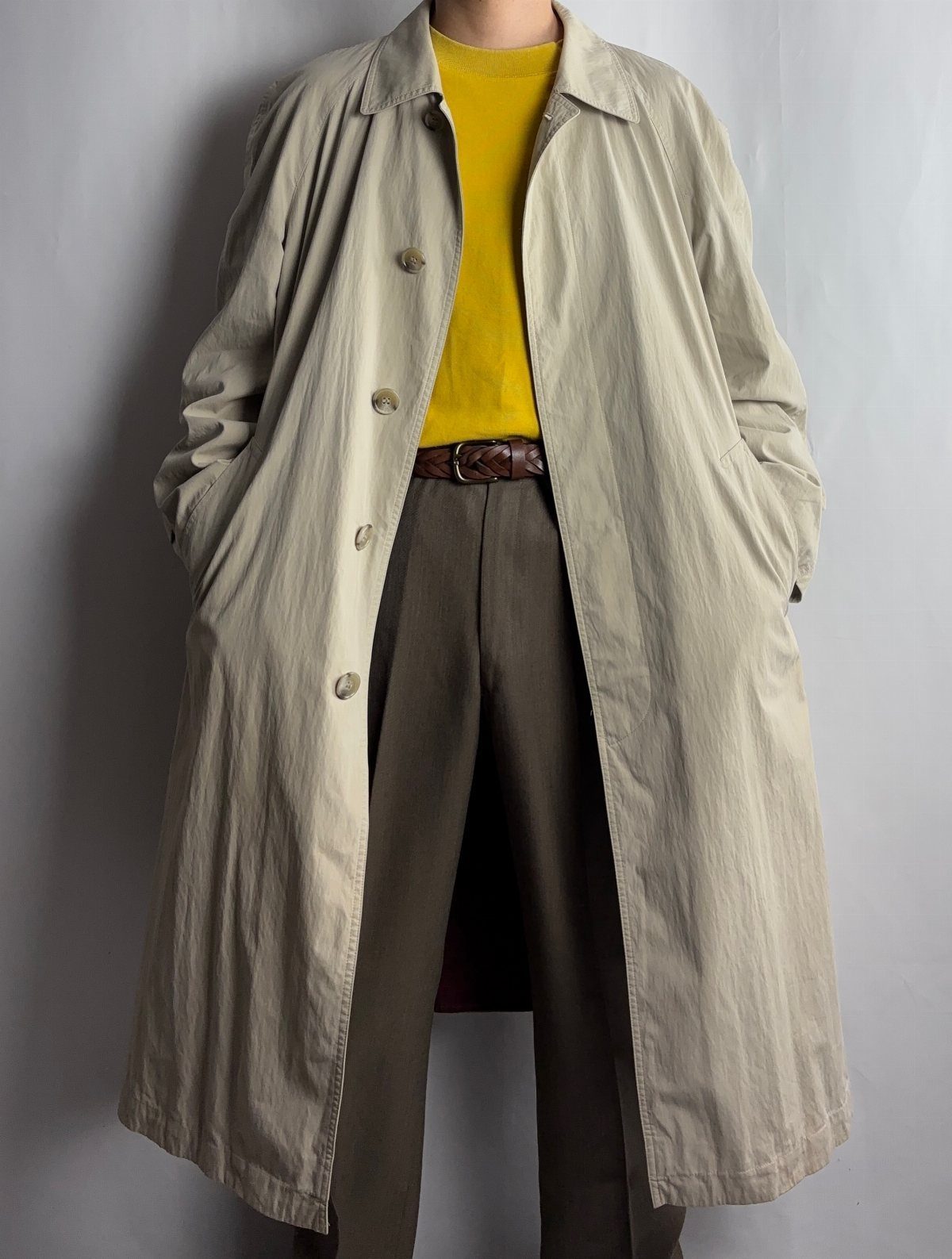 Beige trench coat worn over a yellow shirt and brown trousers.